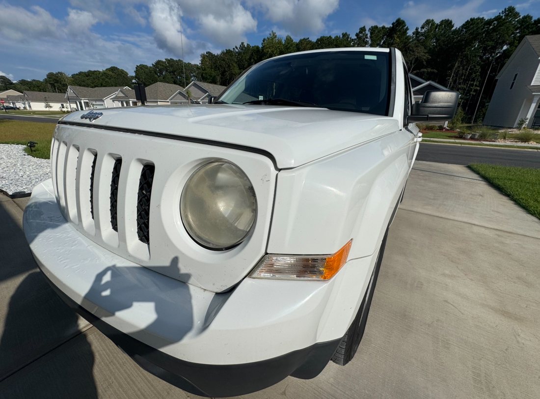 White Jeep Patriot in a Carolina driveway with a clouded, yellowed headlight